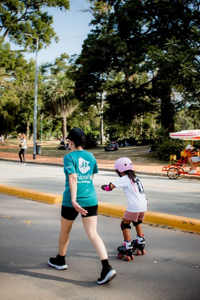 A child in skating gear and an adult walk in the park, promoting a healthy lifestyle.